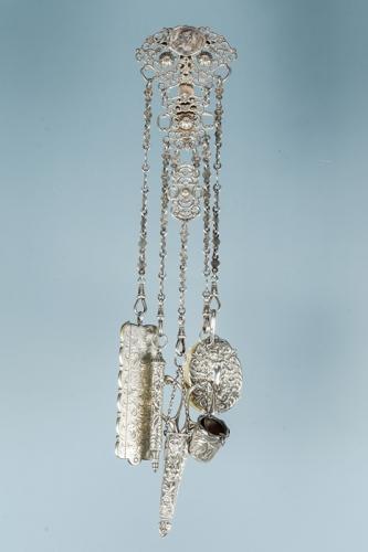 An Edwardian silver Chatelaine, ornate top section with central female medallion above scrolling openwork design, with suspension chains fitted with comb, aide memoir, pencil, thimble holder and scissors in holder, hallmarked: Birmingham, 1902