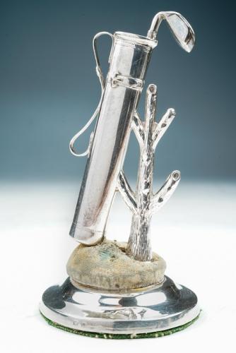 Golfing interest: A George V novelty silver hatpin / desk stand modelled as a golf bag and club resting against a tree on circular stand, by Crissford & Norris, Birmingham 1911, reg no: 504996, 12cm high overall