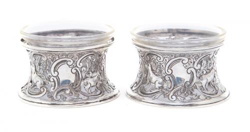 A pair of Victorian silver circular salt dish rings in the Irish manner, the concave bodies chased with various animals and scrolls, with later glass insets, George Nathan & Ridley Hayes, Chester, 1898