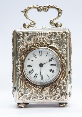 A Victorian silver cased carriage clock, the circular enamel dial with Roman numerals, within a repousse surround foliate, scrolls and bird decoration, rocaille-scroll handle standing on four bun feet, by William Comyns & sons London 1892, French movement, height approx. 70mm x width approx. 53mm x depth approx. 40mm

 Condition: Overall good, hairline to dial, age related marks, small dents to case corners and feet, monogrammed cartouche