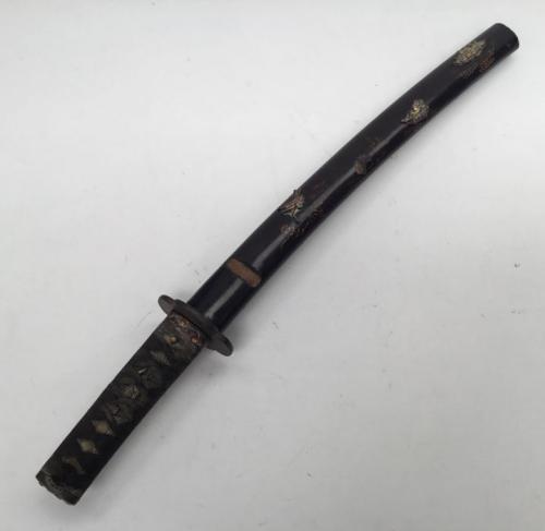 A Japanese Wakizashi short sword.
 Cord Tsuka hilt binding over a ray skin handle, with gilt Menuki ornament to both sides.
 Iron Tsuba with simple chased foliage decoration.
 Copper Sepoa and Habaki.
 Copper Fuchi with flower decoration that matches the Kashira (end cap).
 Steel single edged blade, contained in a lacquered ‘Saya’ scabbard.
 Recess to the scabbard for holding a Kozuka (now absent).
 Tang is signed to both sides, and is plugged in 2 places, which may suggest an older blade.
 Appr