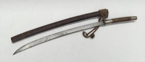 A 19th century Burmese Sword (Dha).
 Rounded wooden grip with white metal pommel and guard.
 Steel slightly curved single edge blade, with false edge near the tip.
 Polished wooden scabbard with multiple wire bindings along its length.
 Rope binding / baldric attached near the throat of the scabbard.
 Approximately 84cm in scabbard, blade length 59.8cm
 Condition: some service wear, notably to the scabbard, which appears to have some of the wire bindings missing.
 Blade is good, with minor dark