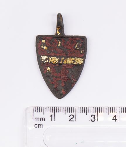 "Medieval Heraldic Mount. Copper-alloy. H30mm. W24mm. 10.37g. The pendant has a red enamel background split horizontal across the middle with a gold gilt band. There are three gold gilt birds across the top section above the gilt band and another three below but almost all the gilt has worn away on these three. This imagery appears to exactly match that used by Roger Beauchamp, 1st Baron Beauchamp of Bletsoe (c. 1315 – 3 January 1380). Beauchamp was was an English soldier and peer who served bot