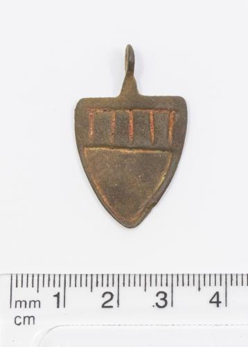 Medieval Heraldic Mount.  Circa, 13th - 14th century AD. Copper-alloy. H26mm. W21.4mm. 4.11.g. A shield style pendant with five vertical lines and two horizontal lines across the top (looks like two letter MM) in red enamel above a recessed shield shape.