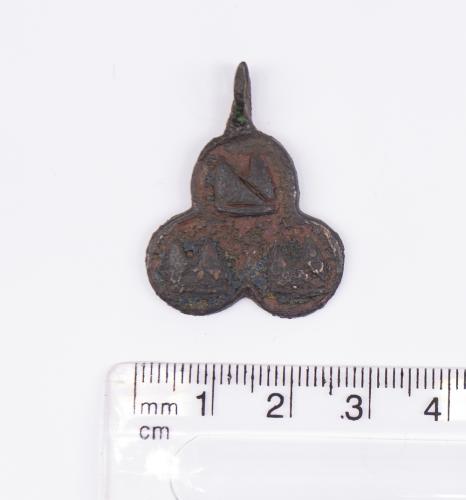 Medieval Heraldic Mount. Copper-alloy. H23.7mm. W24.8mm. 9.07g . The pendant is trefoil in shape with what appears to be the image of a Bishops Mitre in the centre of each of the three rings. The Church connection is backed by the trefoil shape as the word “trefoil” is Latin (trifolium “three leaved plant”) and was used in Christian symbolism.